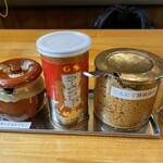 ラーメン食堂オムたす - 卓上の調味料（ヤンニョンジャン、ラーメンコショー、にんにく醤油漬け）