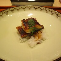 奥 - 青鰻：三河一色産 一年物の青鰻を甘辛く、芳ばしく、ふっくらと焼きたてで岐阜 “はつしも“（白飯）と一緒にいただきます。上には木の芽が添えられています。