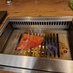 焼肉うしごろ - 赤いタレに漬け込んだ大分県産の特選サーロインを、網の鉄板の上で焼いている様子のその1です。