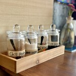 カフェモン - 卓上のタイの調味料クルワンプルーン。
      手前からプリックポン（唐辛子）、ナムターン（きび糖）、プリックソムナム（唐辛子入り酢）、プリックナンプラー（唐辛子入りナンプラー）の4種類が基本。