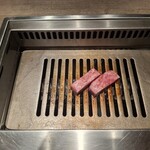 焼肉うしごろ - 熊本県産のA5厚切りサーロインを、網の鉄板の上で焼いている様子のその1です。