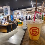 maru5deli Hiroshima T-Site Ten - 黒塗り天井、壁はTシャツやバックや本等が置かれた木製棚、灰色の打ちっぱなしコンクリート床、雑貨が展示された木製展示台、オープンキッチンと木製カウンター、セレクトショップの併設カフェみたいな空間