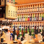 ぬる燗佐藤 - 店内右の壁いっぱいの一升瓶。