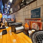 焼肉ホルモン酒場 たかちゃん - 店内は黒塗り剥き出し天井、コンクリート壁&牛のマークとアルファベットの描かれた木板張り壁、灰色の土間コンクリートの床、独り焼き肉に対応した若者向きの雰囲気の焼肉屋さんと言った空間、BGMはJ-POP