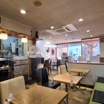 shiki - 店内は白い天井と絵画がポスター等が飾られた白壁、淡いベージュ色の床、テーブルクロスを掛けたテーブルセット、奥側は緑色の長ソファと2席テーブルの組み合わせ、全体的にスッキリとした空間