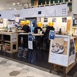 とののベーコン。 - 新幹線口からekie kitchenエリアへ降りるエスカレーターで降りて直ぐ、白い天井、白壁、黒いタイル貼り床、ガラス張りショーケース、立ち飲みエリアは木組のカウンター&木製テーブル、シンプルな空間