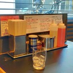 東京油組総本店 - テーブルの卓上、真ん中より右手は食べるラー油風な香辛料に玉ねぎ、お酢、ラー油と配置。後はコショウだったり箸だったり。