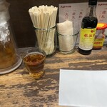 六坊担担面 - 卓上のメンバー。冷たい麦茶と調味料。紙エプロンとお茶はセルフです。