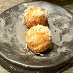 レヴォ - 小さなプチシューの上に削りかけられた山羊のチーズが、まるで初雪のようにふわりと積もり、黒い器の上で静かに輝きます。シュー生地は軽やかで、ひと口かじると中から山羊のチーズのコクと、満寿泉の酒粕が溶け合ったクリームがふわりと広がります。発酵の甘やかな香りが鼻に抜け、乳の酸味と酒粕の深みが交差する瞬間、どこか懐かしい温もりが胸に灯ります。