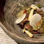 レヴォ - 脇には野草アザミのペーストが濃い緑で添えられ、森の香りとほろ苦さが皿に深みを与える。白いしめじと菊芋の輪切りが土の香りと食感を添え、森の命と火の技術が一皿に凝縮された構成です。