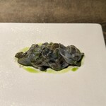 レヴォ - 白い皿の上に灰青色の薄いスライスが折り重なるように並び、その質感はまるで花びらのように繊細。