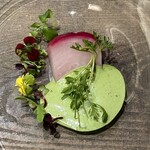 レヴォ - 周囲には緑がかったハーブの乳化ソースが柔らかく広がり、香りと色彩に深みを添える。赤蕪の上にはペッパークレスが一筋立ち上がり、香りにスパイスの緊張感を加える。皿の縁には花や新芽が添えられ、春の兆しや再生の気配を感じさせる佇まいです。