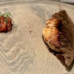 レヴォ - 木のプレートの右側に、炭火でじっくり焼き上げられたサワラが葉に包まれて佇みます。