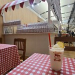 チー坊パーラー - 囲いの壁が無く、白い天井、背後の木板張り壁、木板張り床、屋台の様なKitchenブース、赤&白のチェック柄のテーブルクロスが掛けられた簡単なテーブルセット、BGMは館内放送