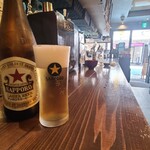 立ち飲み広島 - 店内は灰色の天井、ポスター等が貼られた黒壁&灰色の壁、灰色のタイル貼り床、黄色い提灯&赤い傘等が吊られており、居酒屋さんらしい空間、BGMはJ-POP