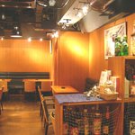 イタリアンカジュアルダイニング何駄感駄 - 入口のボトル棚越しに店内を望む