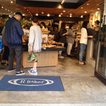 アールベイカー インスパイアード バイ コート ロザリアン - パン陳列台ナナメ置きはどうやら失敗。平行に戻した方がいいがレジ側に寄せても逆側に寄せても使い勝手は悪いままだ。一回り細長くして高さに逃げた方が正解だ。今は低すぎて裾や鞄がパンにこすれるのをよく目撃する