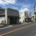 手打うどん 松屋 - 手前の建物がお店で、奥の赤い車は駐車場に入るところ。