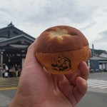 一言堂 - JR高尾駅をバックに「高尾てんぐパン (150円)」