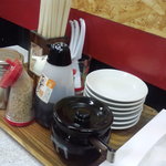 麺通倶楽部 - 卓上には辛子高菜、ゴマ、コショウ、ラー油、餃子タレが置いてある。