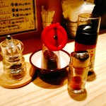 らー油肉つけうどんの南哲 - 卓上にはペッパーミル、白胡麻を黒くなるまで焙煎した深煎り胡麻、風味重視のらー油、一味。