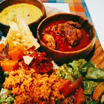 シナモンガーデン - 手前にレタス、トマトの何か、ポルサンボル(ココナツのふりかけ)、赤い辛味ペースト、人参とパインのピクルス。木製のお皿の中には、チキンカレー、黄色い豆カレー。