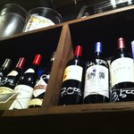 ビストロ酒場マエストロ - テーブル席の上の棚のワインたち。
