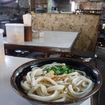 製麺所の仕切りでうどんを受け取り、ダシサーバーでかけうどんにする