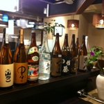 居酒屋 かんなり - カウンターには焼酎のボトルと店主の笑顔が並ぶ。