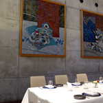 オットセッテ - コンクリート打ちっ放しの壁に、抽象的でダークトーンの絵画が飾られる。対照的に白いテーブルクロスが引き立つ