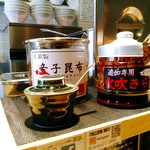 らー油肉つけうどんの南哲 - 卓上にはからーい火吹きらー油、辛くない辛子昆布、生姜。