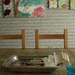 コントン レストラン - 壁には絵が飾ってあります。スプーン、フォーク、ナイフ、箸、紙ナプキンが籠に入っています。