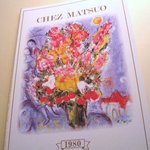 Chez Matsuo - オーナーが書いた絵が表紙のメニュー　店内の所々にはオーナーが書いた絵画が展示されている