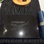 レストランRyu - 店のロゴが描かれた、石のプレートが出迎える。紺色のナフキンは地元の御糸織（みいとおり）
